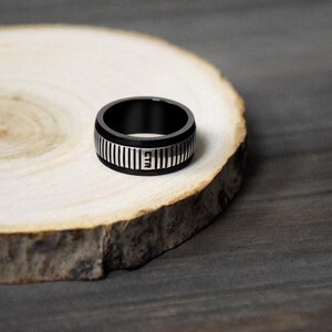May include: A black and silver ring with a textured band and the word "CTR" engraved on the side.