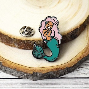 May include: A teal and pink enamel pin of a smiling mermaid with a pink tail and a green tail fin.