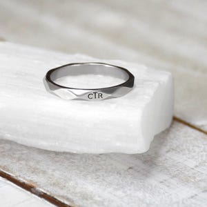 May include: A silver ring with a faceted design and the initials "CTR" engraved on the band.