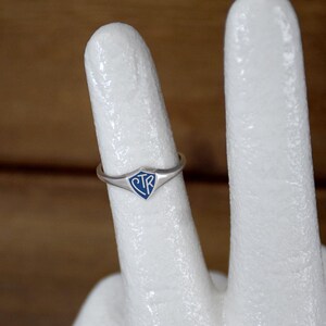 May include: A silver ring with a blue shield-shaped emblem. The emblem features the letters "CTR" in white. The ring is displayed on a white surface, showcasing its design and details.