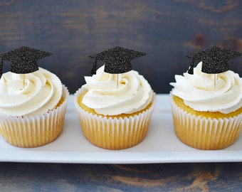 May include: Three vanilla cupcakes with black glitter graduation caps on top. The cupcakes are on a white rectangular plate.