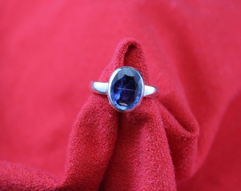 May include: A silver ring with a dark blue oval gemstone set in the centre.