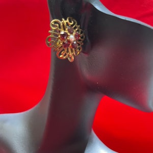 May include: Gold tone earrings with a floral design and purple and white rhinestones.