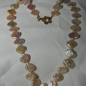 Puede incluir: Un collar hecho de perlas irregulares iridiscentes con un cierre de oro. Las perlas son una mezcla de blanco, rosa y crema.