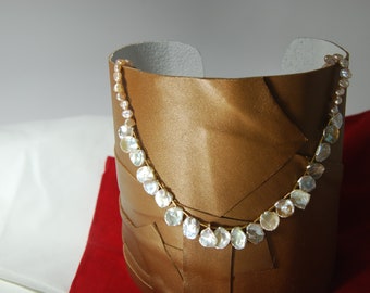 May include: A gold necklace with white and pink pearl-like beads. The necklace is displayed on a brown leather background.