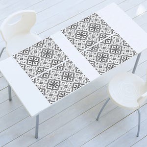 May include: Four black and white patterned placemats on a white table with two white chairs.