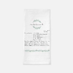 May include: A white kitchen towel with a handwritten recipe for Ice Box Chocolate Pie. The recipe includes ingredients like sugar, cocoa, cornstarch, vanilla, and salt. The towel is decorated with a green olive branch design.