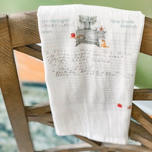 May include: A white tea towel with a vintage stove and cat illustration. The towel has handwritten text that reads "Recipe from the kitchen of:" and a recipe for "Sponge Cake" with ingredients and instructions.