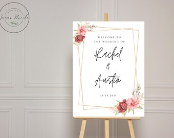 Op de afbeelding: Een wit welkomsbord voor een bruiloft met een gouden frame en bloemmotieven. Het bord staat "Welkom op de bruiloft van Rachel & Austin 10.16.2024".