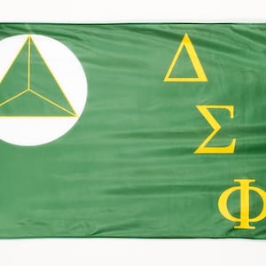 May include: A green flag with a white circle containing a yellow triangle in the center. The letters Delta Sigma Phi are written in yellow on the right side of the flag.
