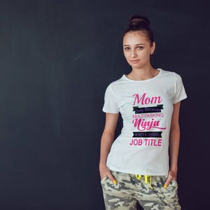 May include: White t-shirt with the text "Mom Only Because Multitasking Ninja Is Not A Official Job Title" in black and pink lettering.