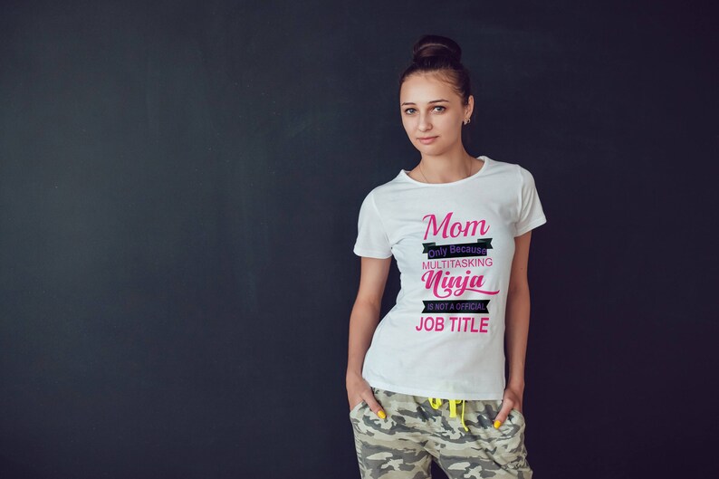 May include: White t-shirt with the text "Mom Only Because Multitasking Ninja Is Not A Official Job Title" in black and pink lettering.