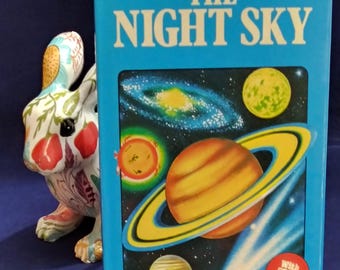 Puede incluir: Un libro azul con el título "Spotter's Guide to The Night Sky" con una imagen de planetas y estrellas. El libro incluye cartas estelares.
