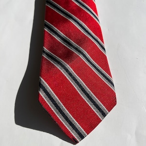 Puede incluir: Una corbata de rayas rojas y negras con punta puntiaguda.