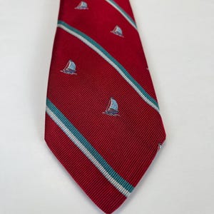 Puede incluir: Una corbata de seda roja con rayas blancas y azul verdoso y un patrón repetido de pequeños veleros.