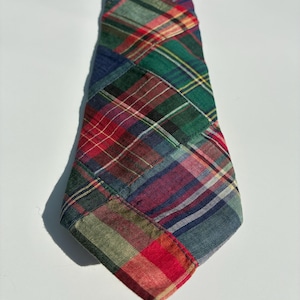 May include: A necktie constructed from a patchwork of various plaid fabric patterns. The design features a mix of green, red, blue, and yellow tartan squares stitched together, creating a multi-colored, textured appearance across the entire surface.