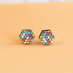 Può includere: Un paio di orecchini in legno a forma di cubo di Rubik. Gli orecchini sono dipinti in una varietà di colori, tra cui rosso, arancione, giallo, verde, blu e bianco.