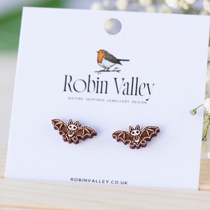 Peut inclure: Une paire de boucles d'oreilles en bois en forme de chauve-souris avec un motif de cr&acirc;ne blanc. Les boucles d'oreilles sont sur une carte blanche avec le texte "Robin Valley" et "Nature Inspired Jewellery Design".