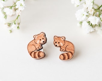 Puede incluir: Un par de pendientes de madera con un diseño de panda rojo. Los pendientes están hechos de madera natural y tienen un acabado marrón.