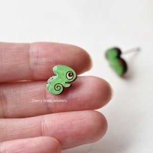 Könnte beinhalten: Ein Paar grüne Chamäleon-Ohrringe aus Holz. Die Ohrringe sind klein und haben ein süßes, cartoonartiges Design.