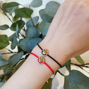 May include: Two friendship bracelets with gold smiley face charms. One bracelet is red and the other is black.