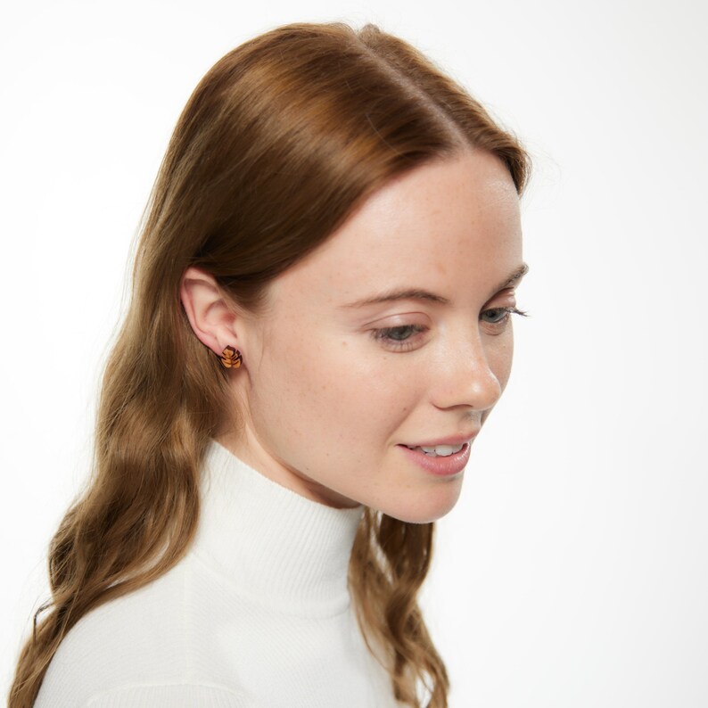 May include: A woman wearing a white turtleneck sweater with a pair of small, brown, flower-shaped earrings.