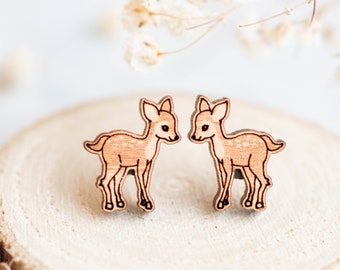 May include: A pair of wooden earrings featuring a cute deer design. The earrings are made of natural wood and have a light brown color.