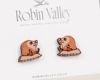 May include: A pair of wooden earrings featuring a cute cartoon mole peeking out of its burrow. The earrings are made by Robin Valley, a nature-inspired jewelry design company.