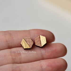 May include: A pair of hexagonal wooden earrings with a gold geometric design. The earrings are a light brown color with gold accents.