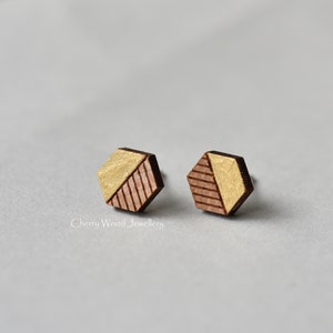 May include: A pair of geometric wooden earrings with a gold and brown color scheme. The earrings are hexagonal in shape and have a geometric pattern.