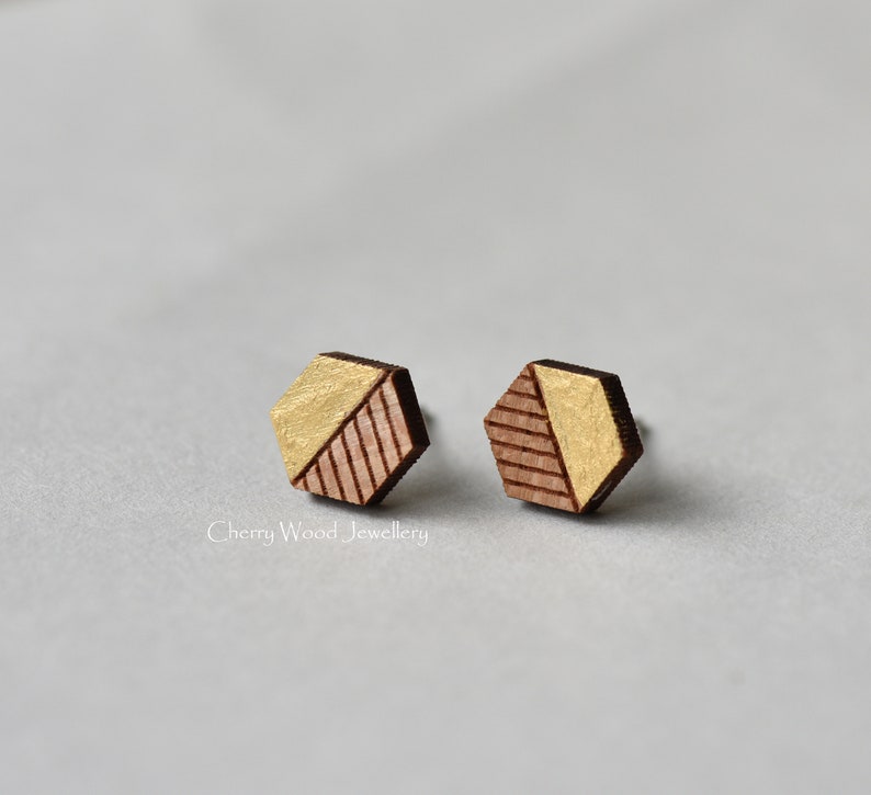 May include: A pair of geometric wooden earrings with a gold and brown color scheme. The earrings are hexagonal in shape and have a geometric pattern.