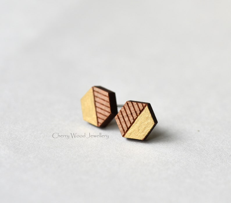 May include: A pair of geometric wooden earrings with a gold and brown color scheme. The earrings are hexagonal in shape and have a diagonal line design.