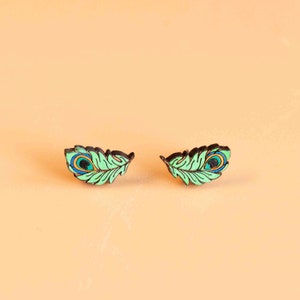 May include: A pair of green and blue peacock feather earrings. The earrings are made of wood and have a detailed design.
