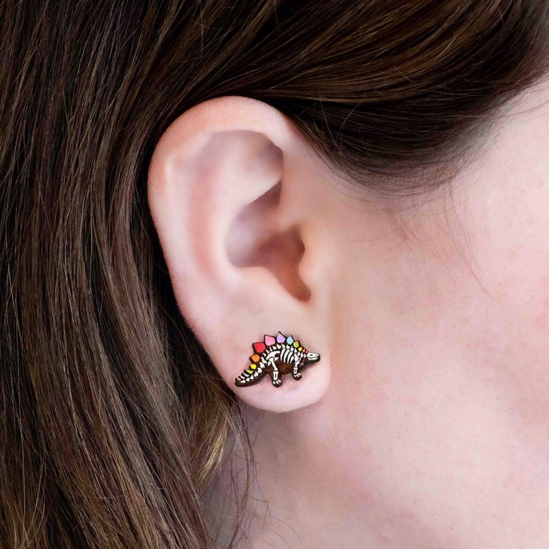 May include: A pair of colorful dinosaur skeleton earrings. The earrings are made of wood and feature a rainbow-colored design.