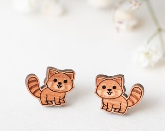 Puede incluir: Un par de pendientes de madera con un diseño de panda rojo de dibujos animados. Los pendientes son marrones y tienen una expresión linda y sonriente.