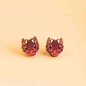 May include: A pair of red dragon head earrings made of wood. The earrings have a cartoon-like design with large eyes and a small mouth.