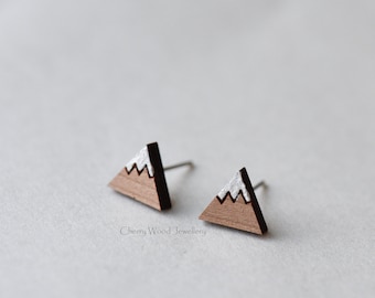 May include: A pair of wooden earrings shaped like a mountain with a white snow cap. The earrings are made of cherry wood and have silver posts.