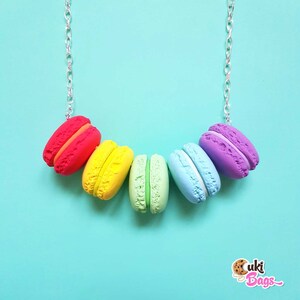 Pode incluir: Um colar de macarons arco-&iacute;ris com uma corrente prateada. Os macarons s&atilde;o vermelho, amarelo, verde, azul e roxo.