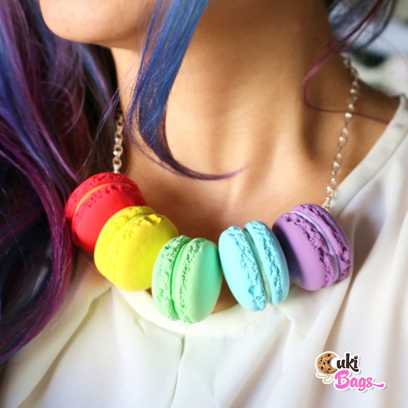Pode incluir: Um colar de macarons coloridos com uma corrente prateada. Os macarons est&atilde;o dispostos em ordem de arco-&iacute;ris, come&ccedil;ando com vermelho, amarelo, verde, azul e roxo.