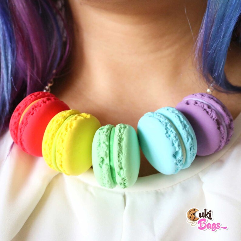 Pode incluir: Um colar de macarons arco-&iacute;ris com macarons vermelhos, amarelos, verdes, azuis e roxos. Os macarons s&atilde;o feitos de argila polim&eacute;rica e s&atilde;o enfiados em uma corrente prateada.
