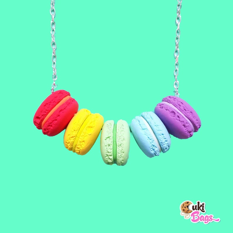 Pode incluir: Um colar de macarons arco-&iacute;ris com uma corrente prateada. Os macarons s&atilde;o vermelho, amarelo, verde, azul e roxo.