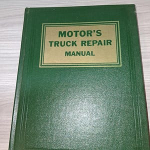 Puede incluir: Un libro verde de Motor's Truck Repair Manual. La portada presenta un recuadro rectangular dorado con el título en letras mayúsculas negras en negrita. El libro está cerrado y sobre una superficie clara.