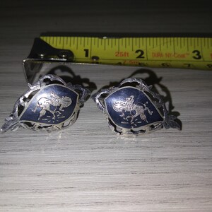 May include: A pair of silver earrings with a blue enamel design. The earrings feature a stylized bird design.