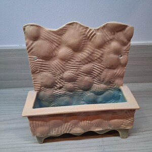 Op de afbeelding: Een decoratieve keramische plantenbak met een textuurontwerp dat op schelpen lijkt, in tinten bruin en blauw. De plantenbak heeft een rechthoekige basis met een geschulpte rand en een hoge, golvende achterkant. Voor kleine planten.