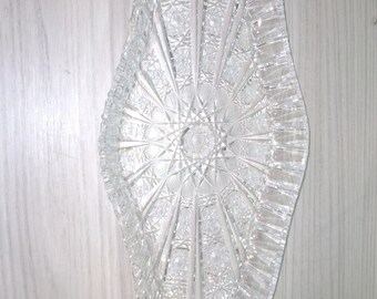 May include: A clear glass serving dish with a decorative, cut-glass pattern. The dish is oval shaped and has a raised rim.
