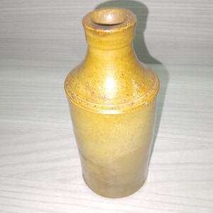 May include: A brown ceramic ink bottle with a rounded body and a narrow neck. The bottle has a slightly textured surface.