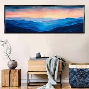 a large painting of a mountain landscape with a colorful sunset sky above. The painting is hanging on a wall above a wooden table with a vase and a book.