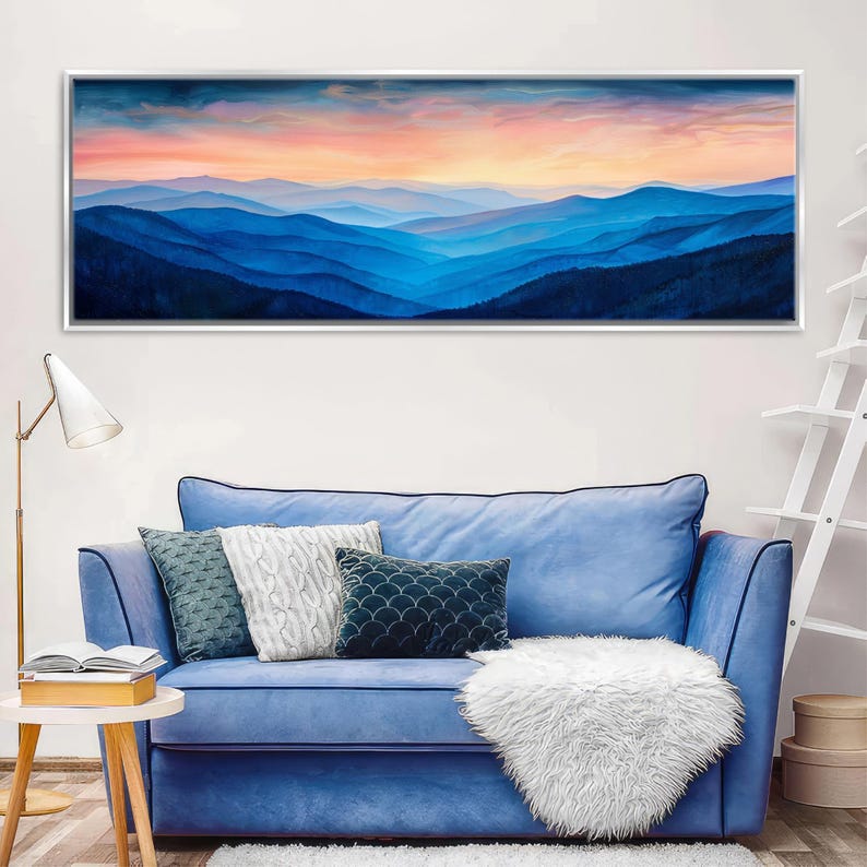 a blue sofa with white throw pillows, a white shag rug, and a framed landscape painting depicting a mountain range at sunset.