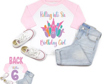 May include: White and pink baseball tee shirt with a rainbow bowling pin graphic and the text "Rolling into Six Birthday Girl". The back of the shirt has a purple number six and the name "Stella".