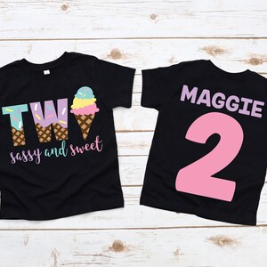 Pu&ograve; includere: Due magliette nere con un design a forma di cono gelato. La parte anteriore di una maglietta dice "TWO sassy and sweet" e la parte posteriore dell'altra maglietta dice "MAGGIE 2".